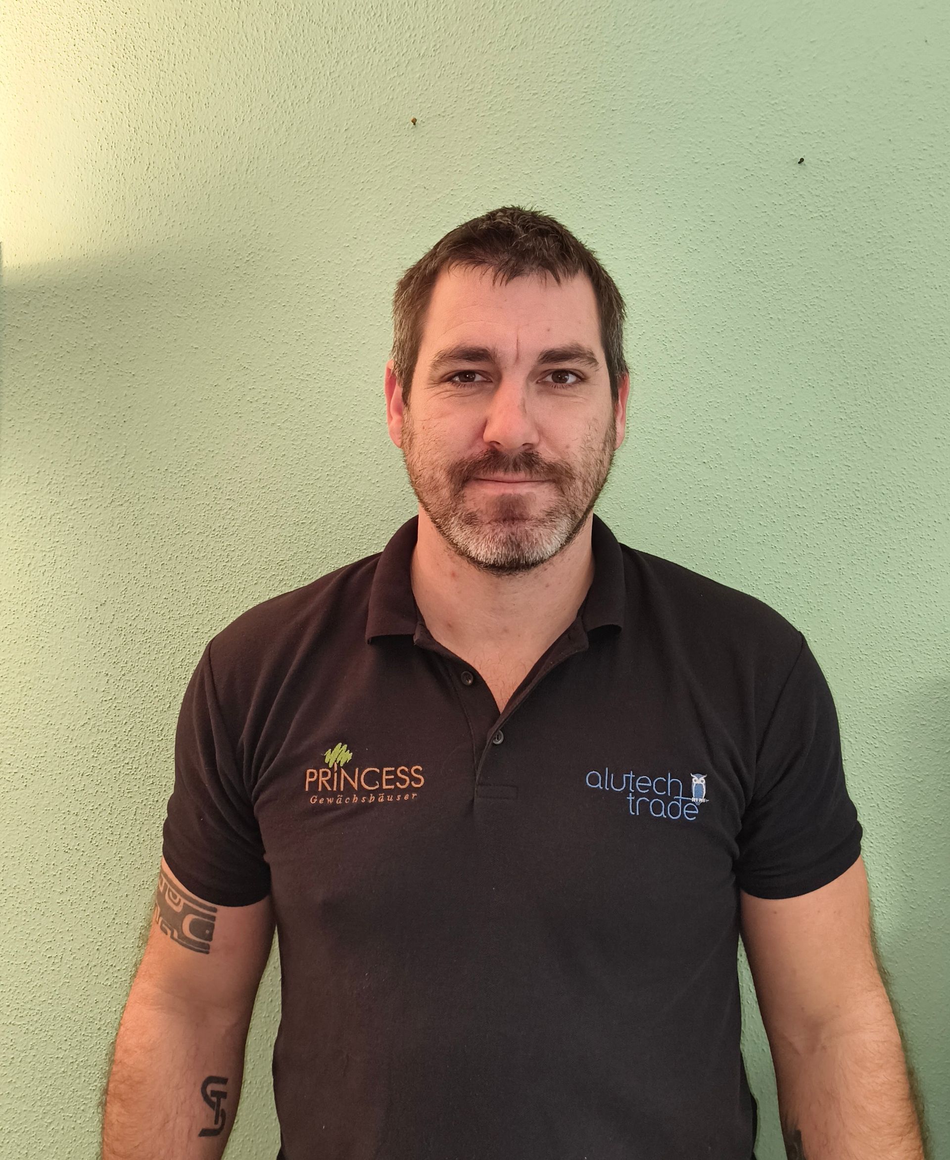 Frau mit Brille und langen Haaren in einem schwarzen Hemd posiert vor einer grünen Wand.