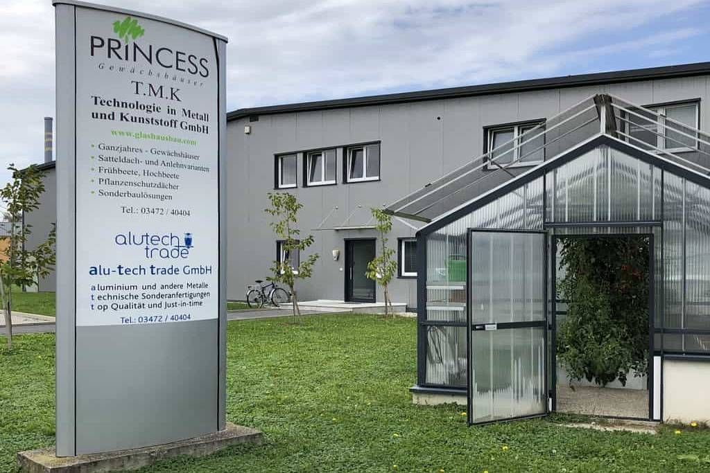 Schild für Prinzessin TSK neben einem Gewächshaus und einem Gebäude auf grünem Rasen.