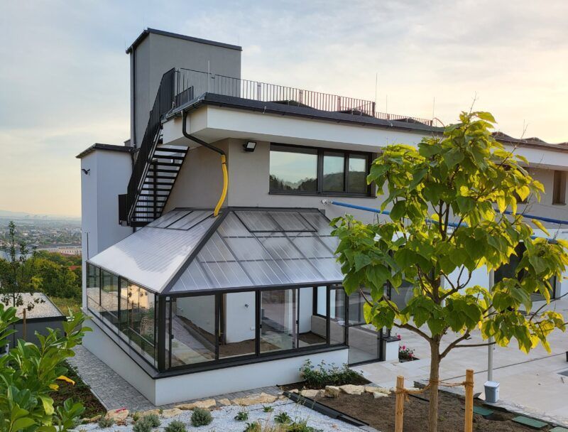 Modernes Haus mit gläsernem Wintergarten, Außentreppe und Dachterrasse.