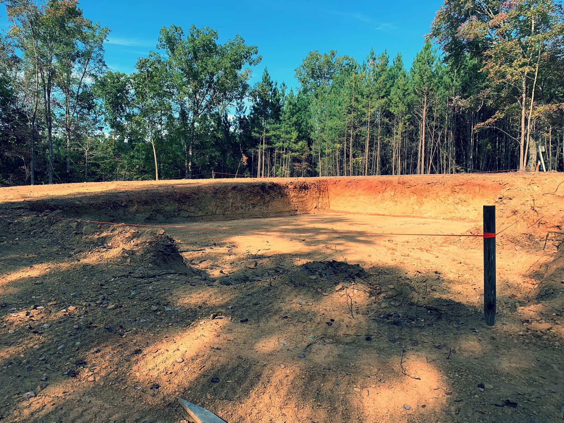 Brown dirt field with a small ditch, trees in the background, blue sky.