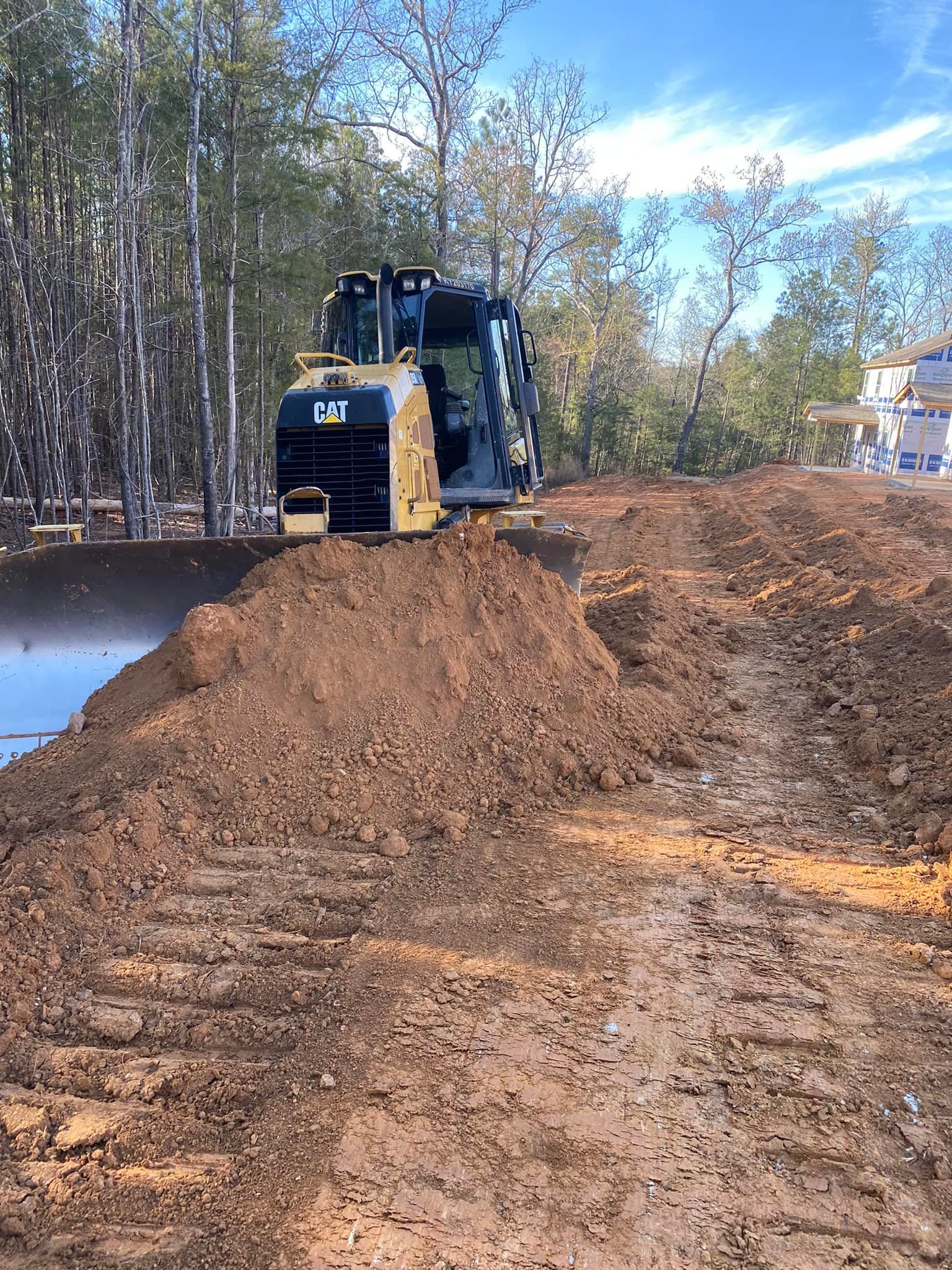 CAT skid steer pushing dirt on a construction site; trees in the background.