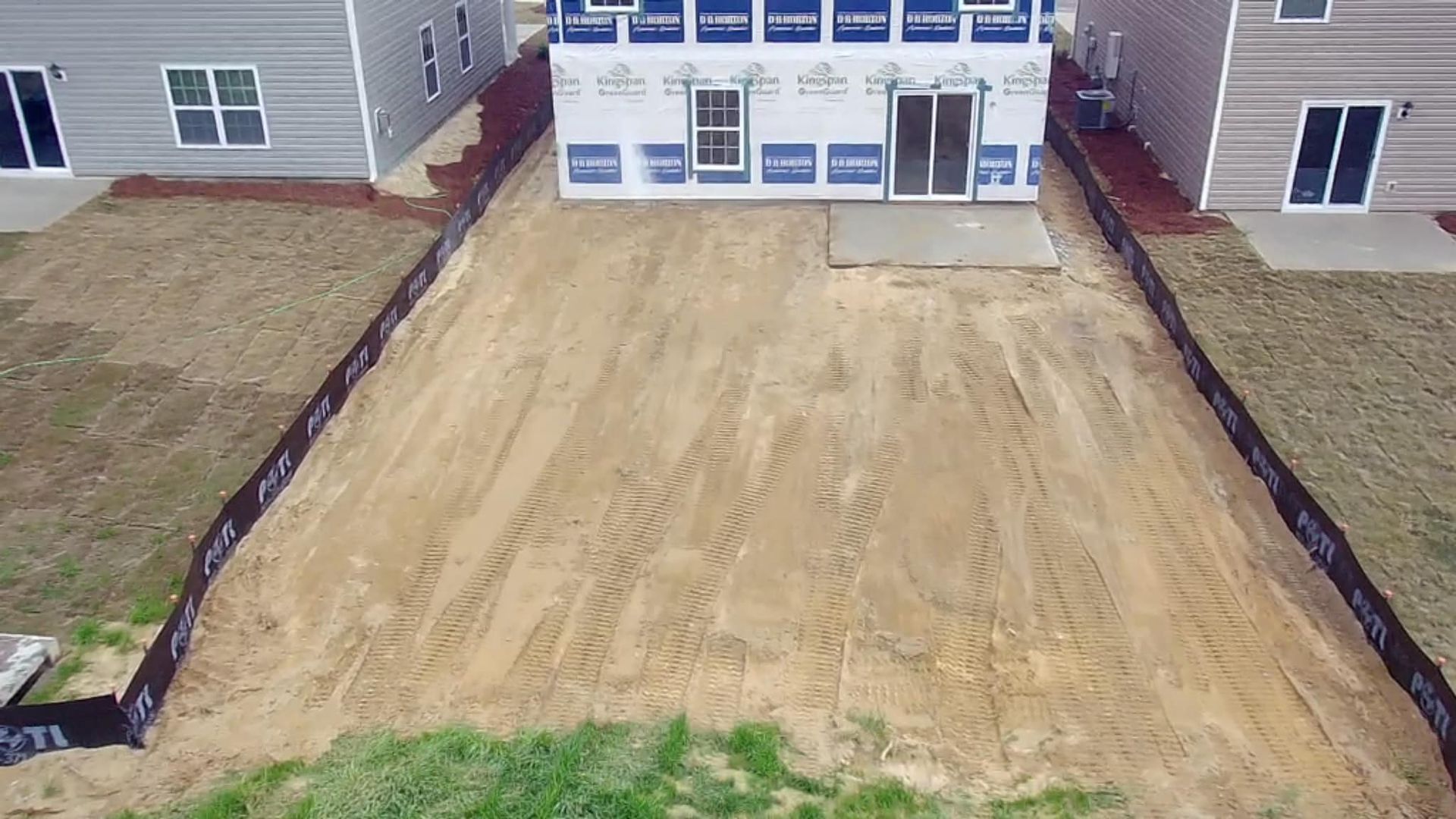 A construction site with a new house, surrounded by dirt and black fencing.