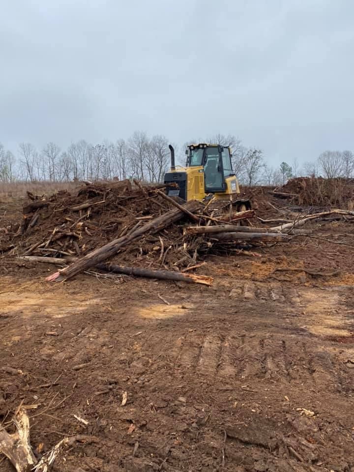 Yellow bulldozer on a pile of wood and debris clearing land, overcast sky.