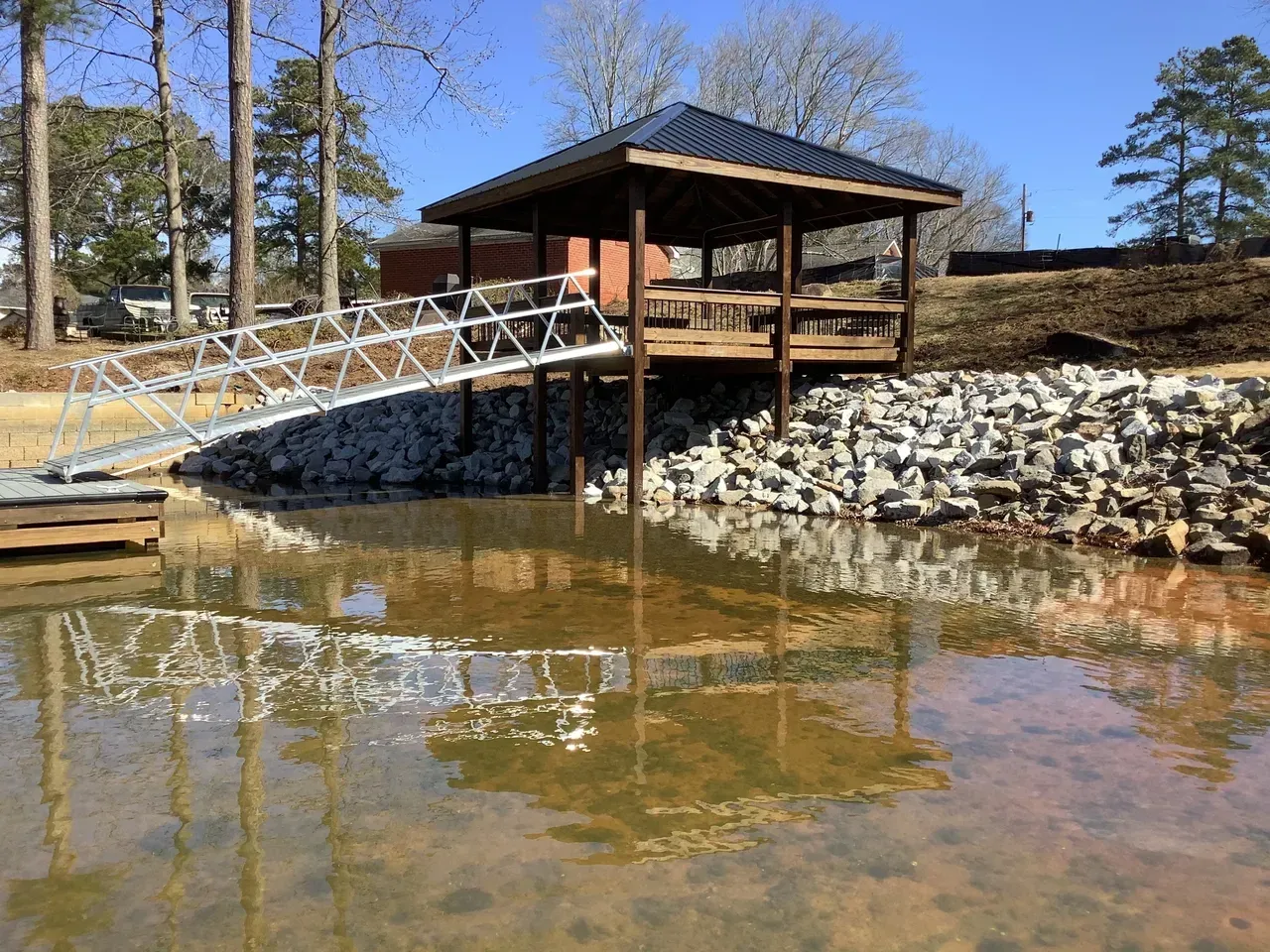 Wooden dock and gazebo over water, accessed by a metal ramp. Rock retaining wall.