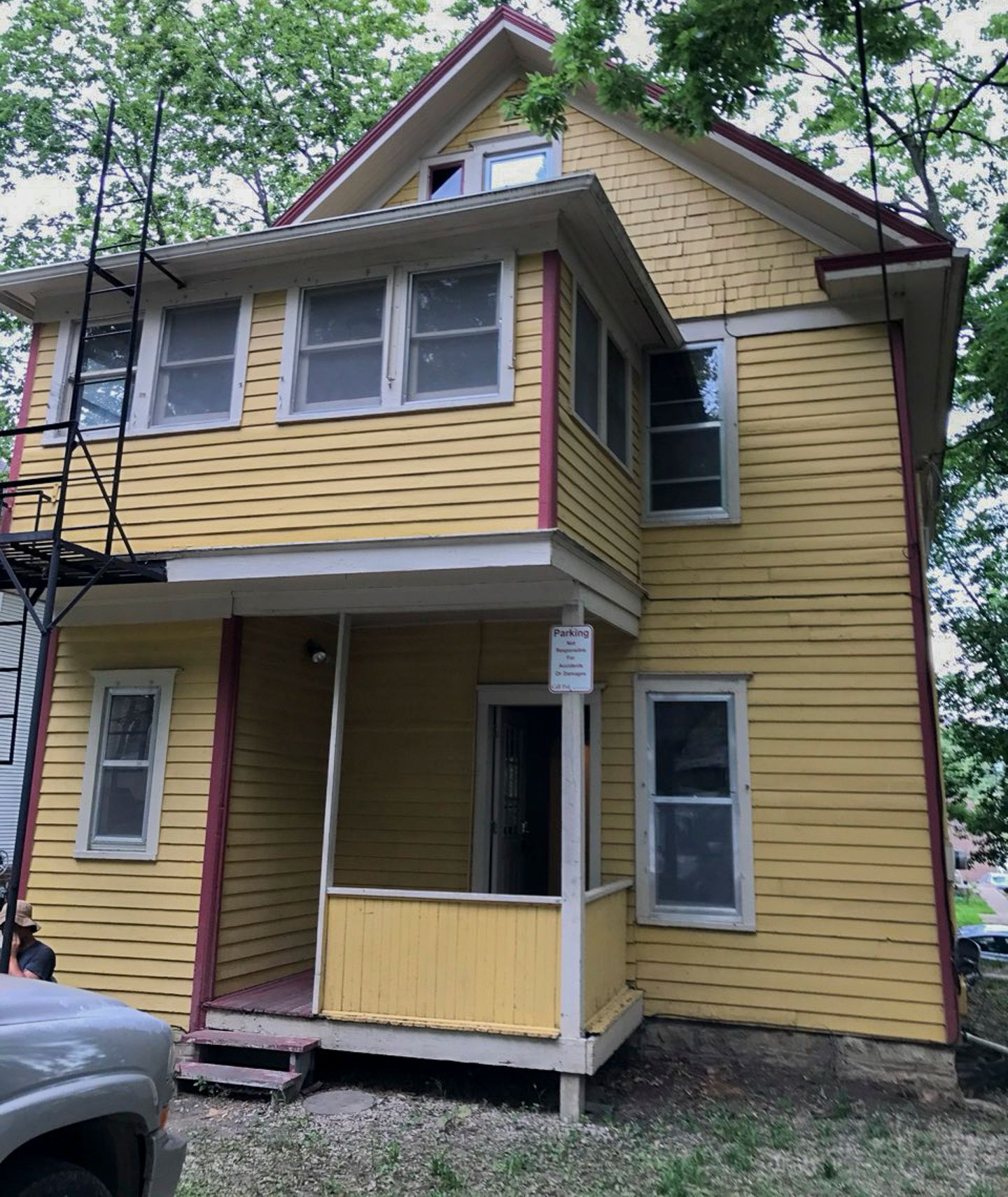 Yellow two-story house with red trim, small porch, and scaffolding on the left.