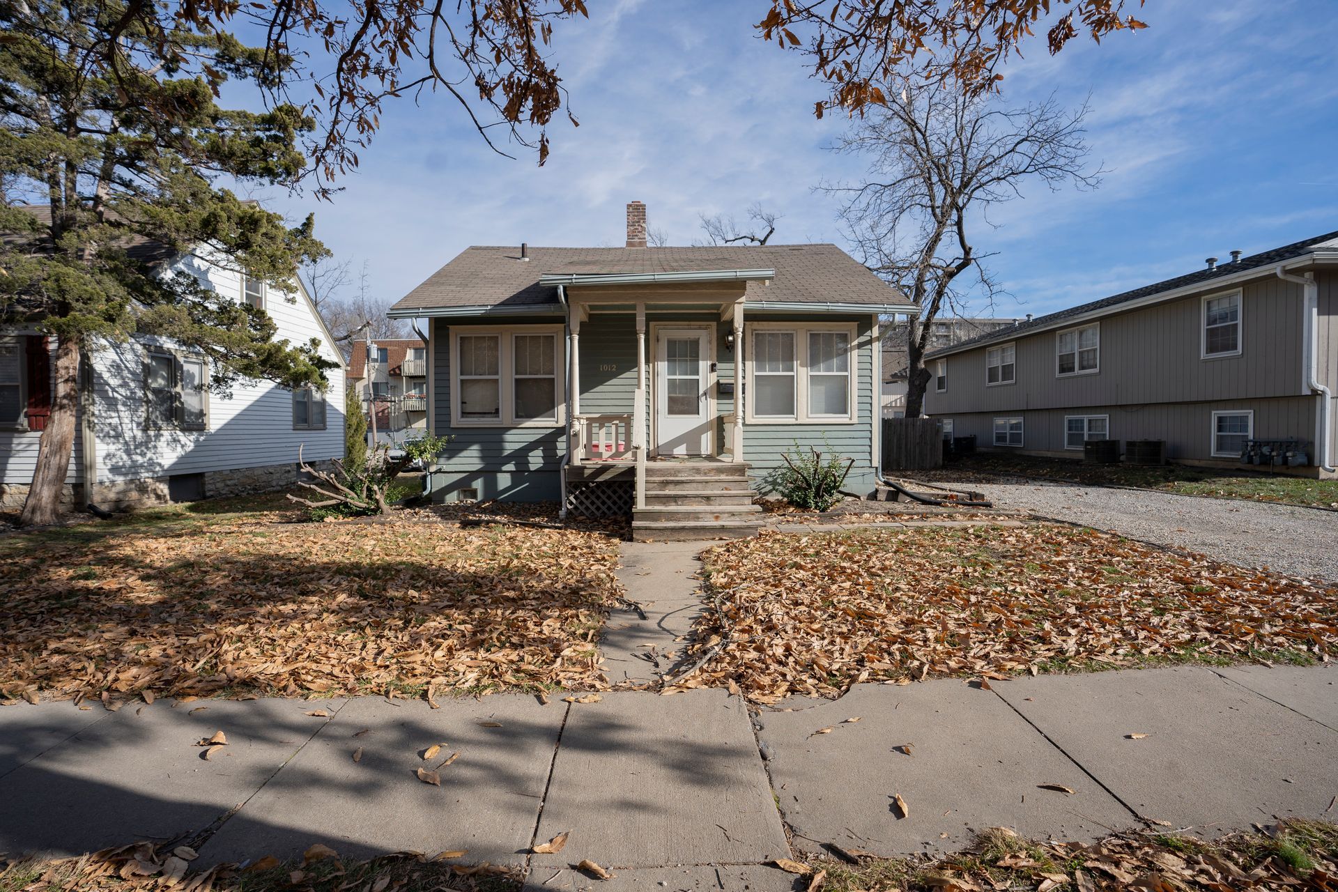 Blue house with a small porch, fallen leaves on the lawn.