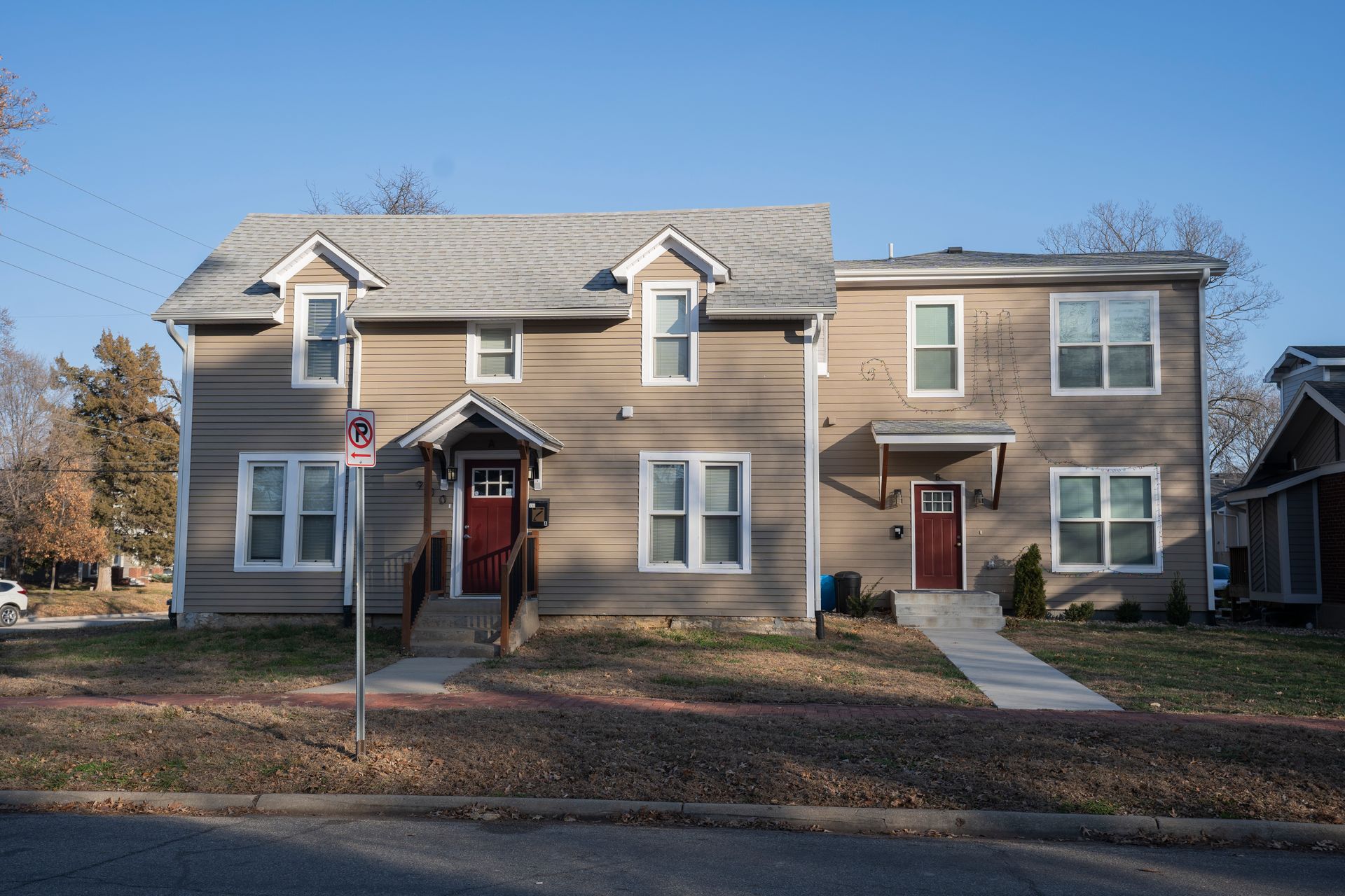 Two-story tan buildings with red doors, set in a residential area, on a sunny day.