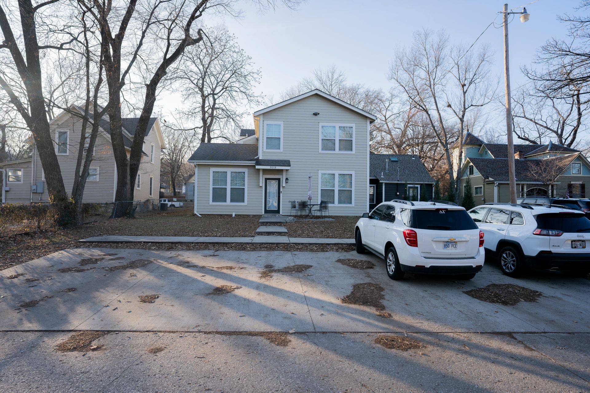 Two-story gray house with cars parked in front; leafless trees on a sunny day.