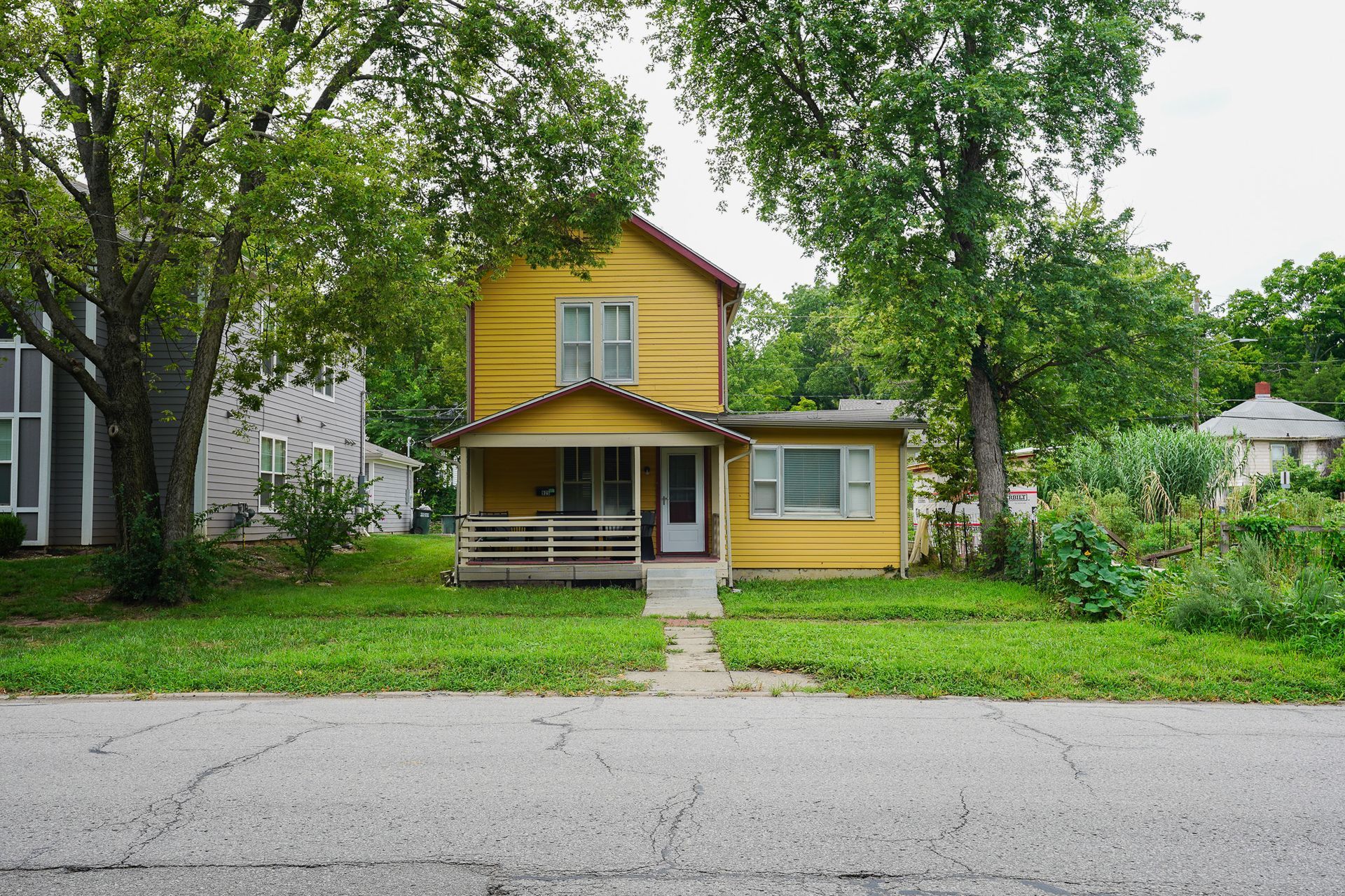 Yellow house with porch, trees, and a garden.