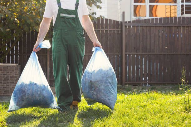 A Man Is Carrying Two Bags Of Trash In A Backyard — Aiken, NC — Aiken Junkmaster