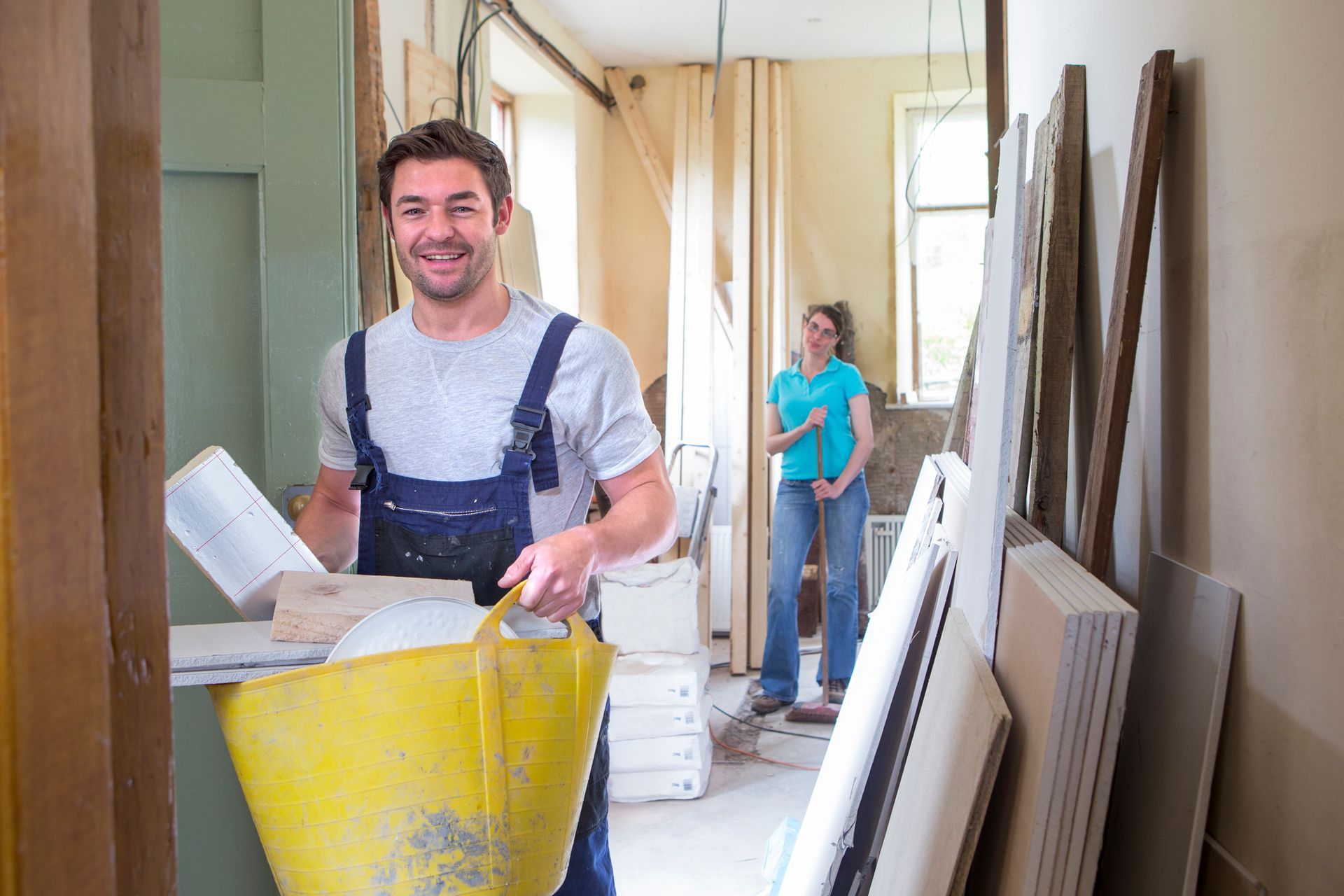 A Man Is Carrying A Yellow Bag Of Cement In A Room — Aiken, NC — Aiken Junkmaster