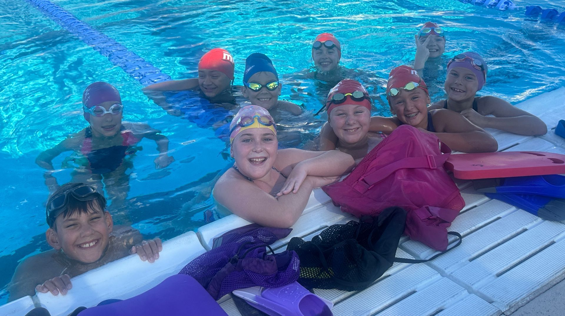Younger swimmers smiling in the water after a practice.