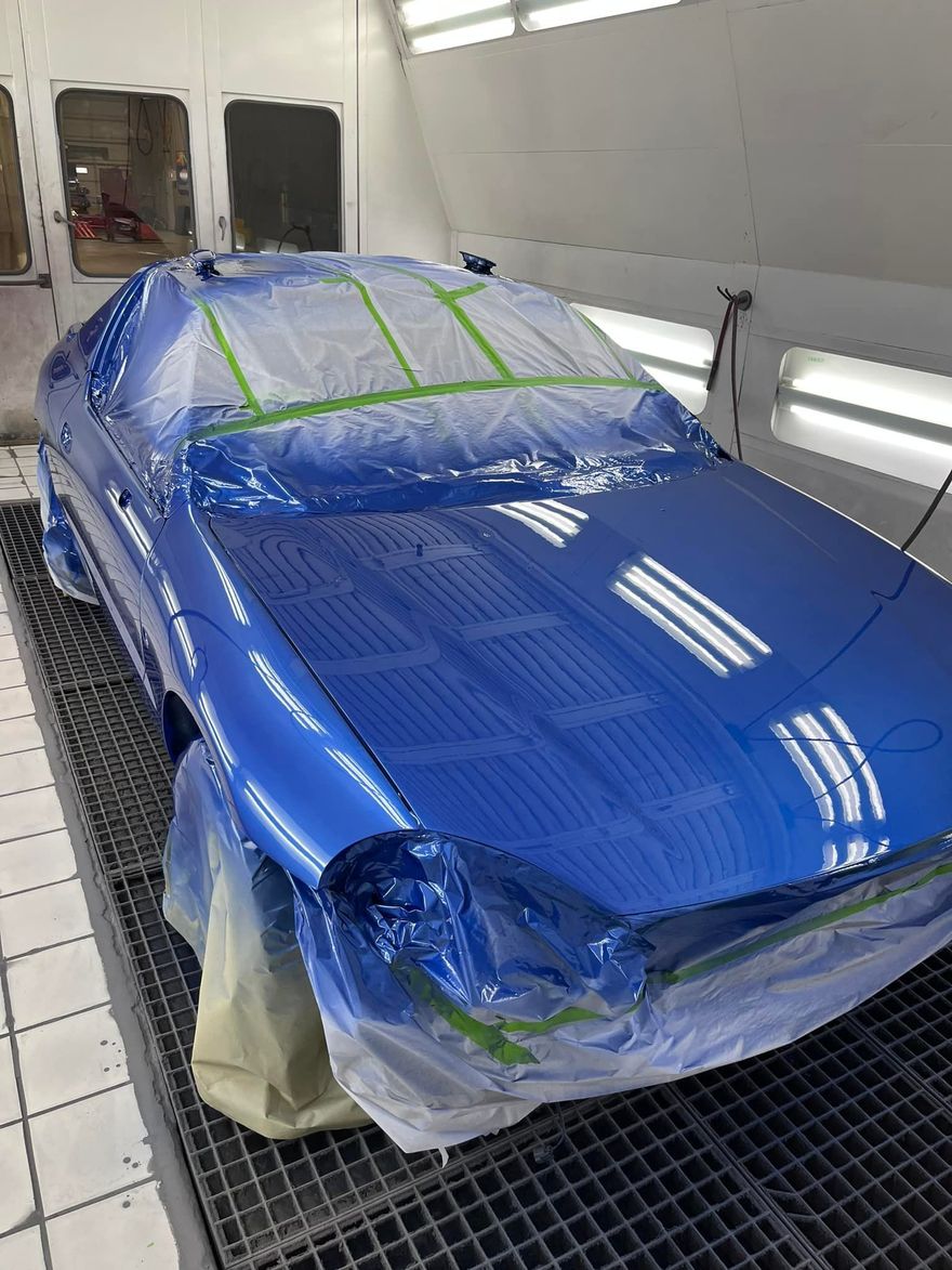 Blue car in a paint booth, taped for protection.