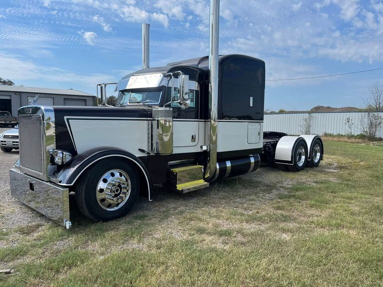 Black, white, and chrome semi-truck on grass field, under a blue sky.