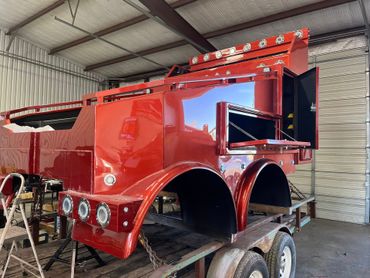 Red custom truck bed with open storage compartments, on a trailer inside a workshop.