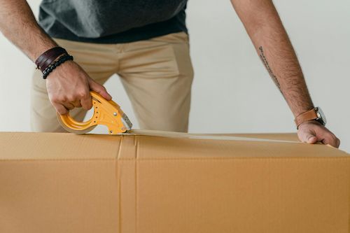 Person using a tape dispenser to seal a cardboard box.