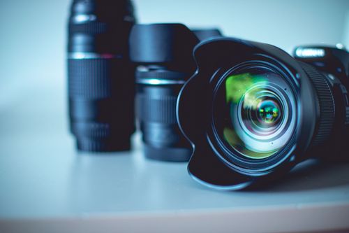 Camera and multiple lenses on a table, with the camera lens in focus, reflecting green and yellow light.