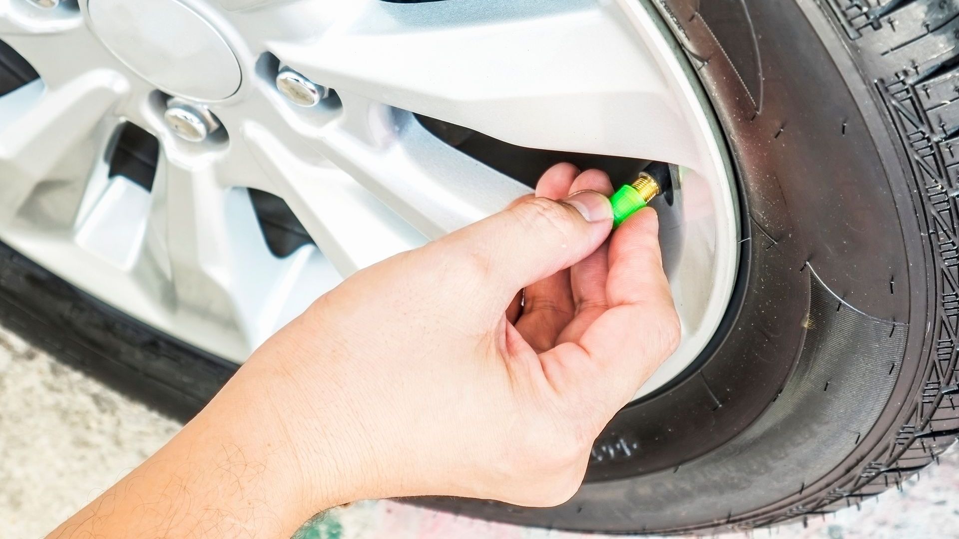 Close up of a hand unscrewing the valve cap on a car wheel