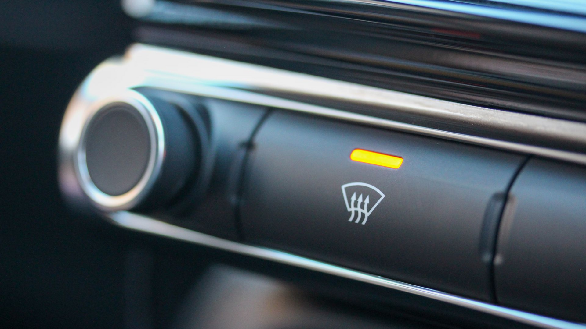 Close up image of a hand scraping ice off the front windscreen using a plastic scraper. 