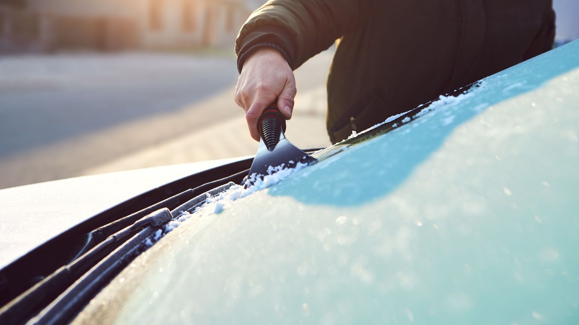 Close up image of a hand scraping ice off the front windscreen using a plastic scraper. 