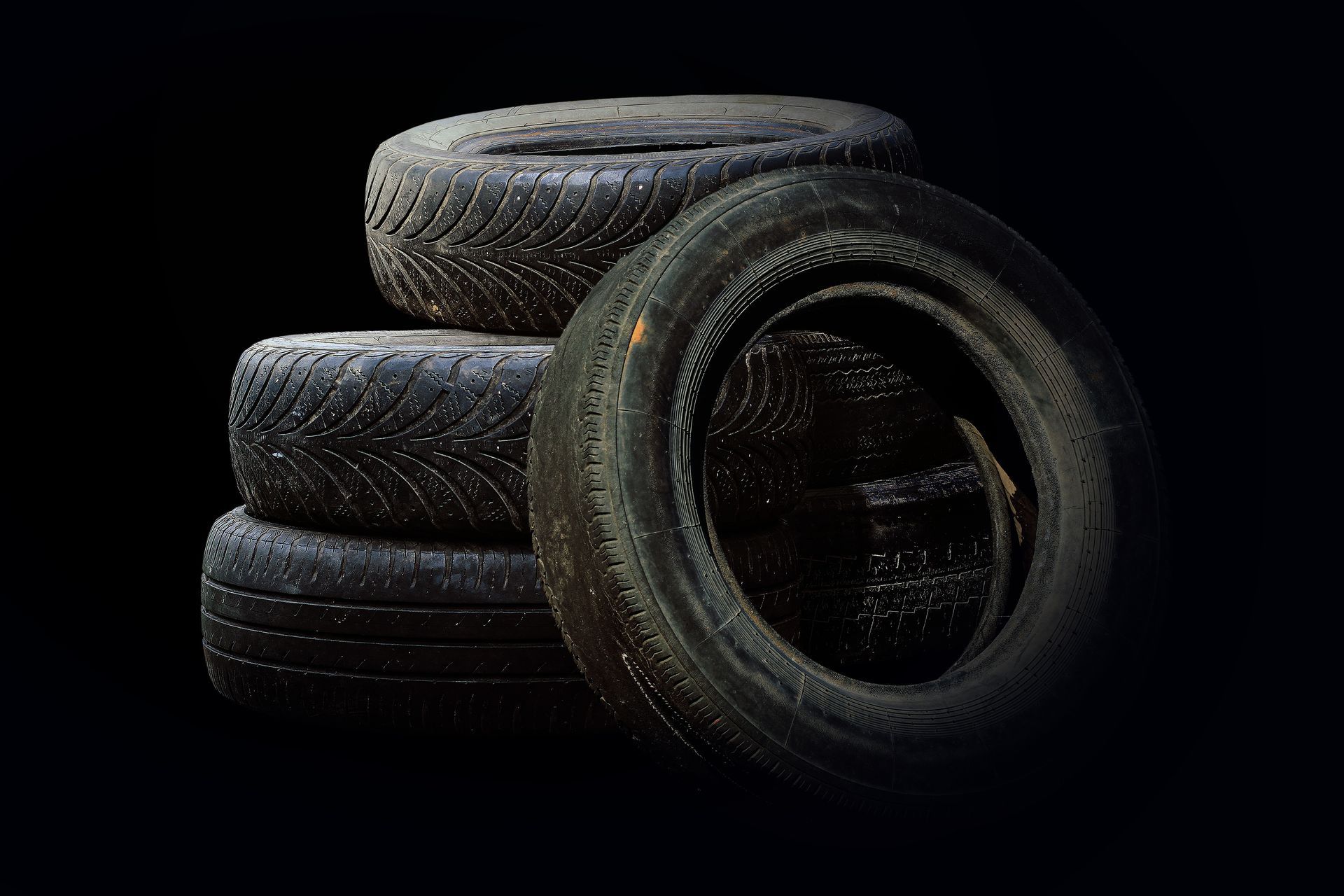 a stack of tyres against a black background. the tyres look used and dirty. 