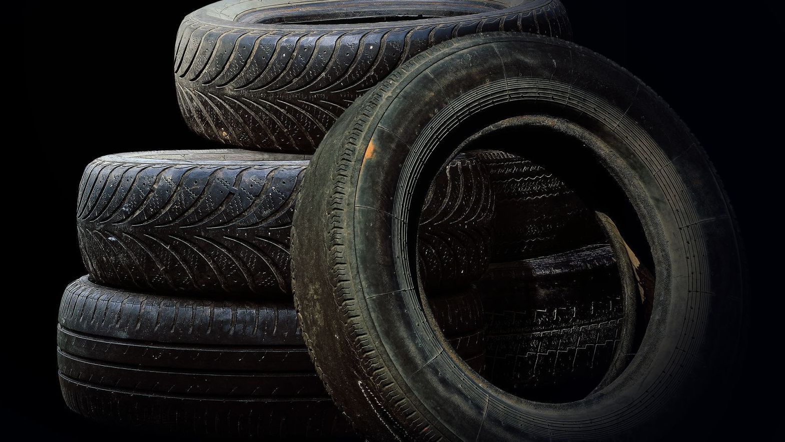 stack of tyres against a black background; the tyres look worn and used