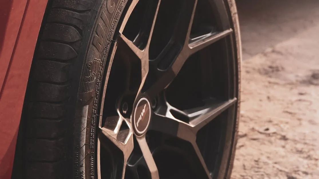 Close up image of a Michelen tyre on a red vehicle. The road in the background looks dusty.