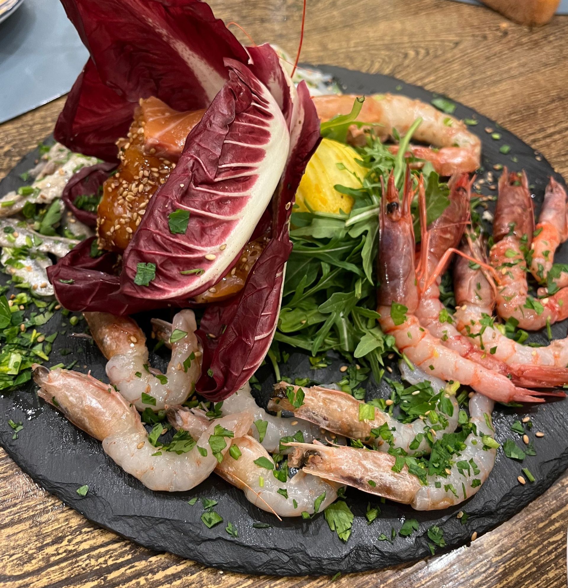 Un piatto di gamberi, lattuga e altre verdure su un tavolo di legno.