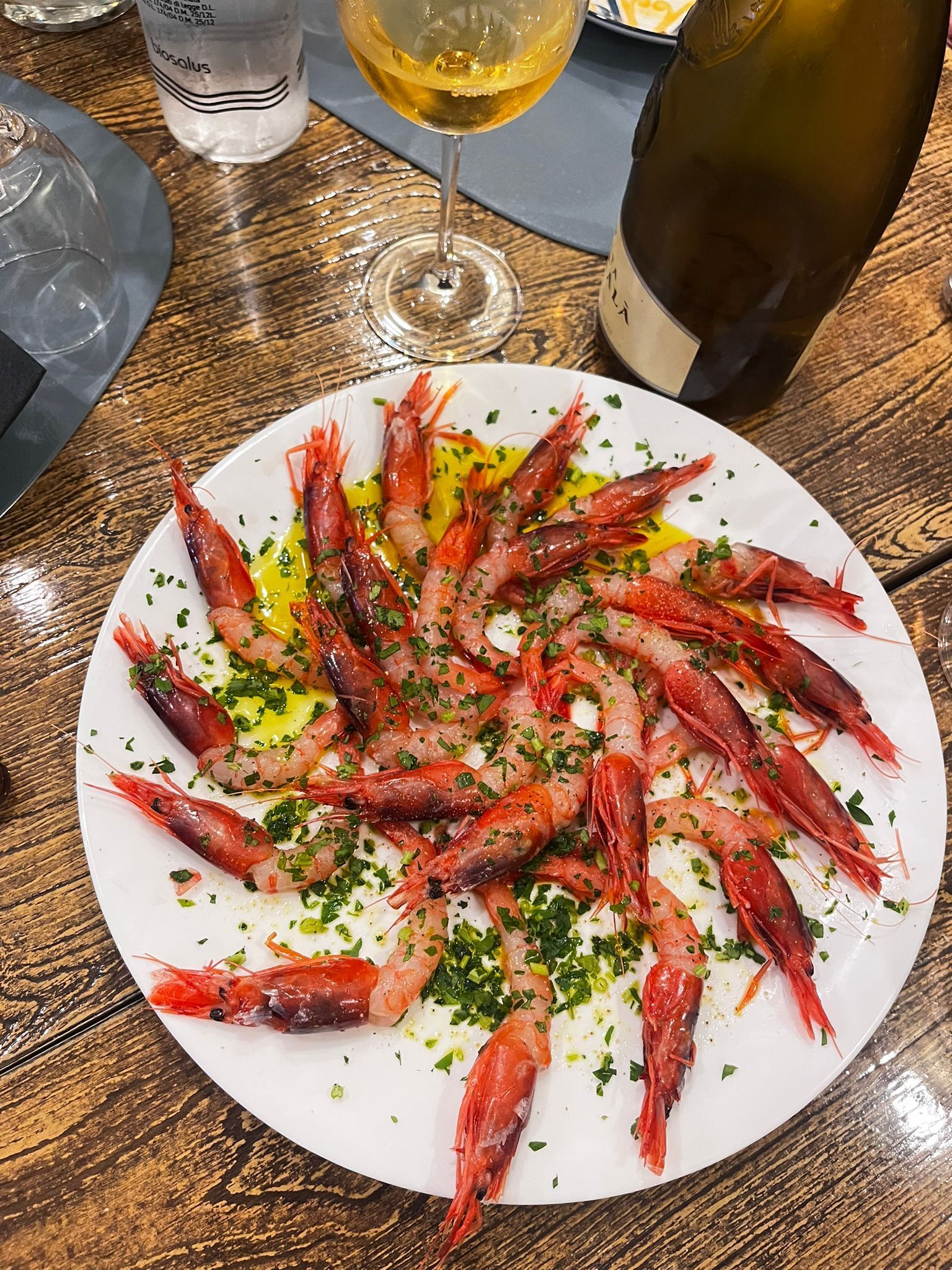 Un piatto di gamberi e un bicchiere di vino su un tavolo di legno.