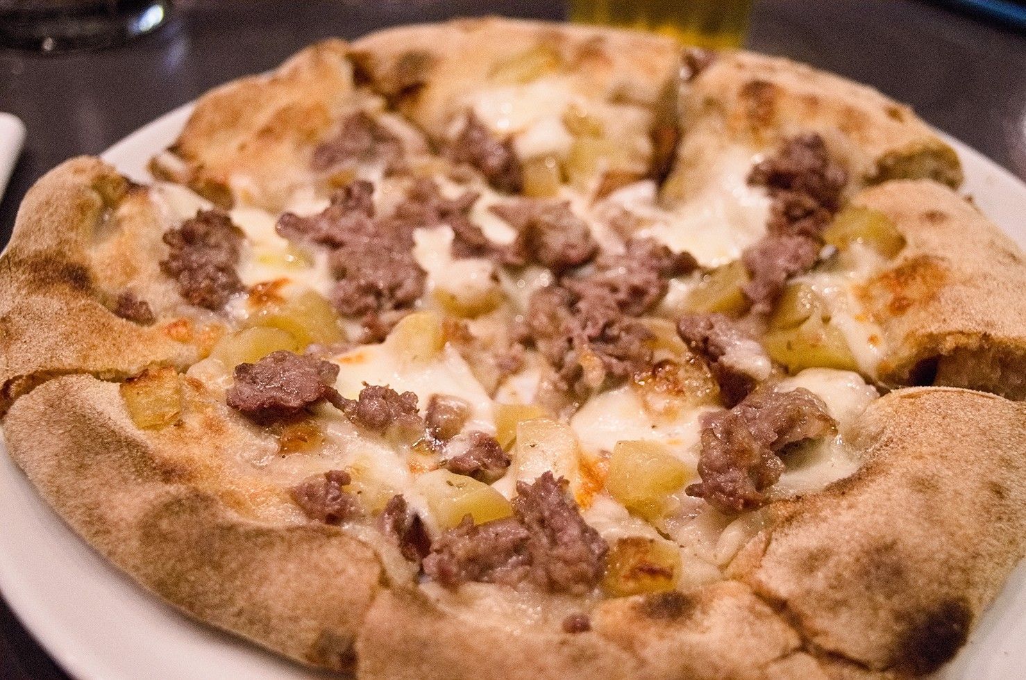 Una pizza con carne e formaggio su un piatto bianco.