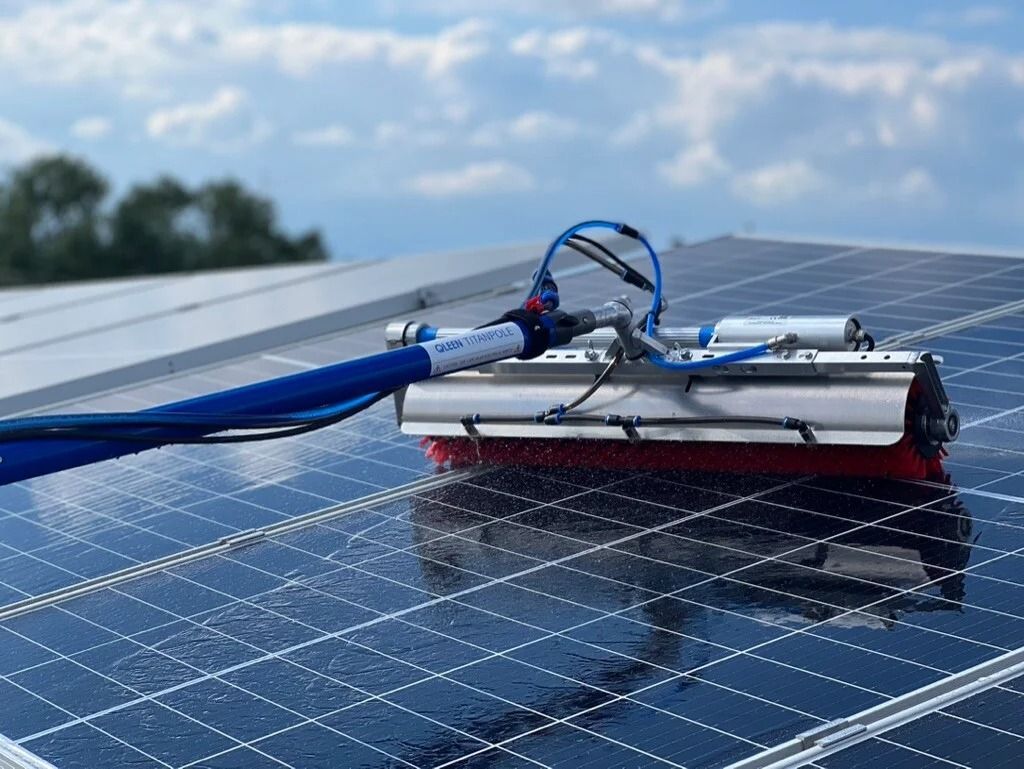 Pannello solare pulito con una spazzola automatica dotata di tubo blu, all'aperto in una giornata nuvolosa.