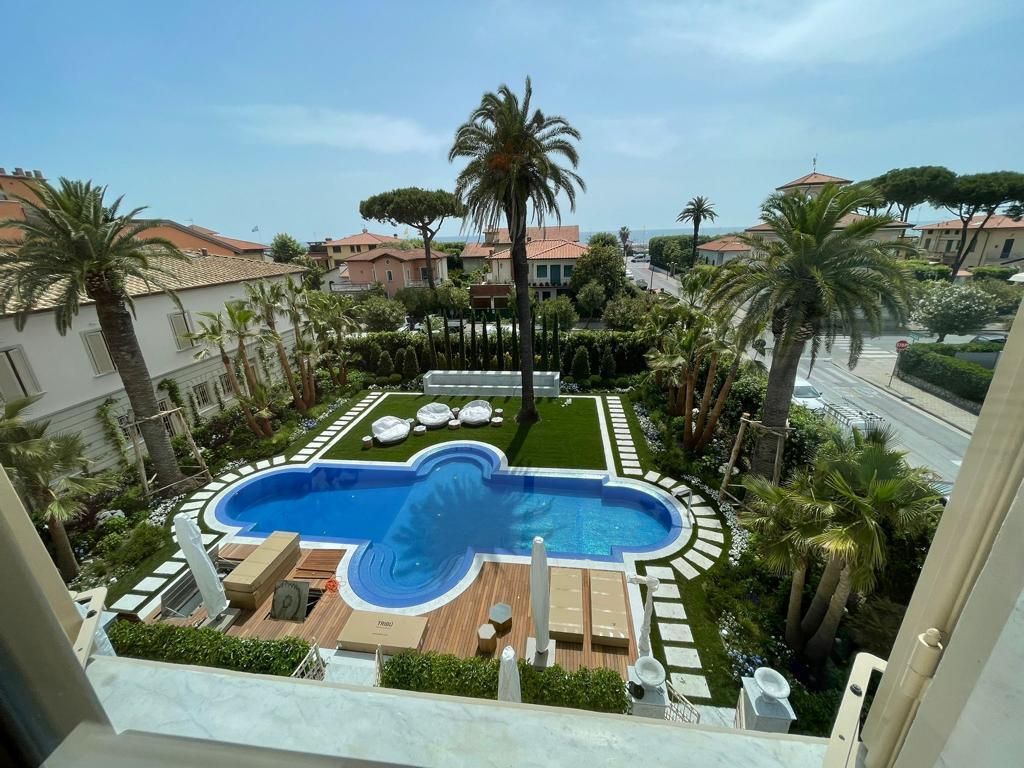 Piscina con palme, prato ed edifici adiacenti. Giornata di sole.