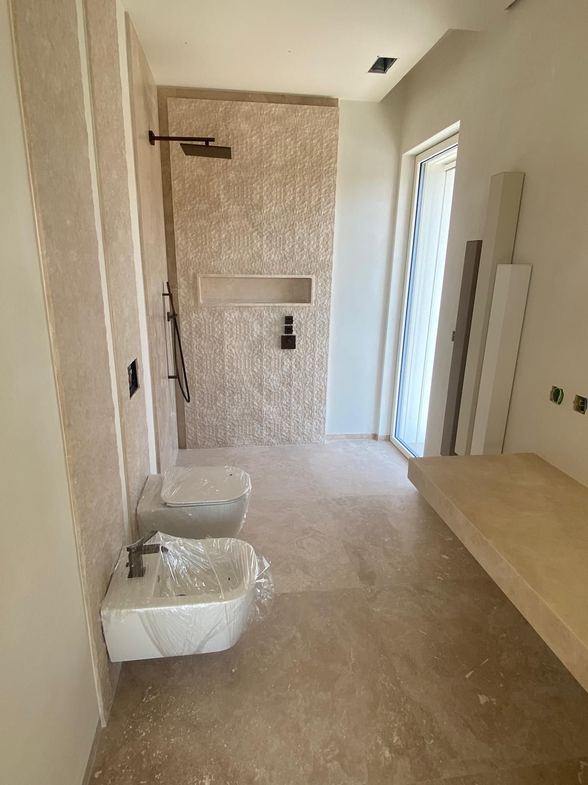 Bagno in costruzione, con zona doccia, WC e bidet. Piastrelle e pareti beige.