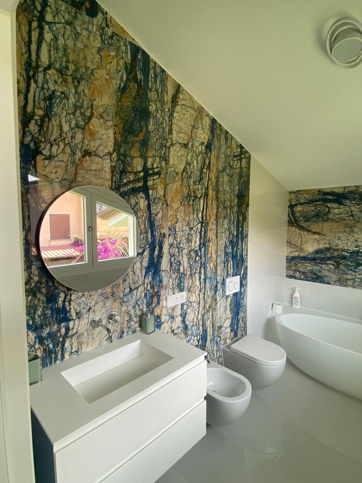 Bagno moderno con carta da parati con motivo a roccia, sanitari bianchi, specchio rotondo e vasca da bagno.