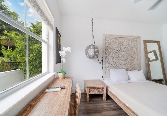 Bedroom with a large window, wooden furniture, and decorative headboard, featuring white walls and a light-colored floor.