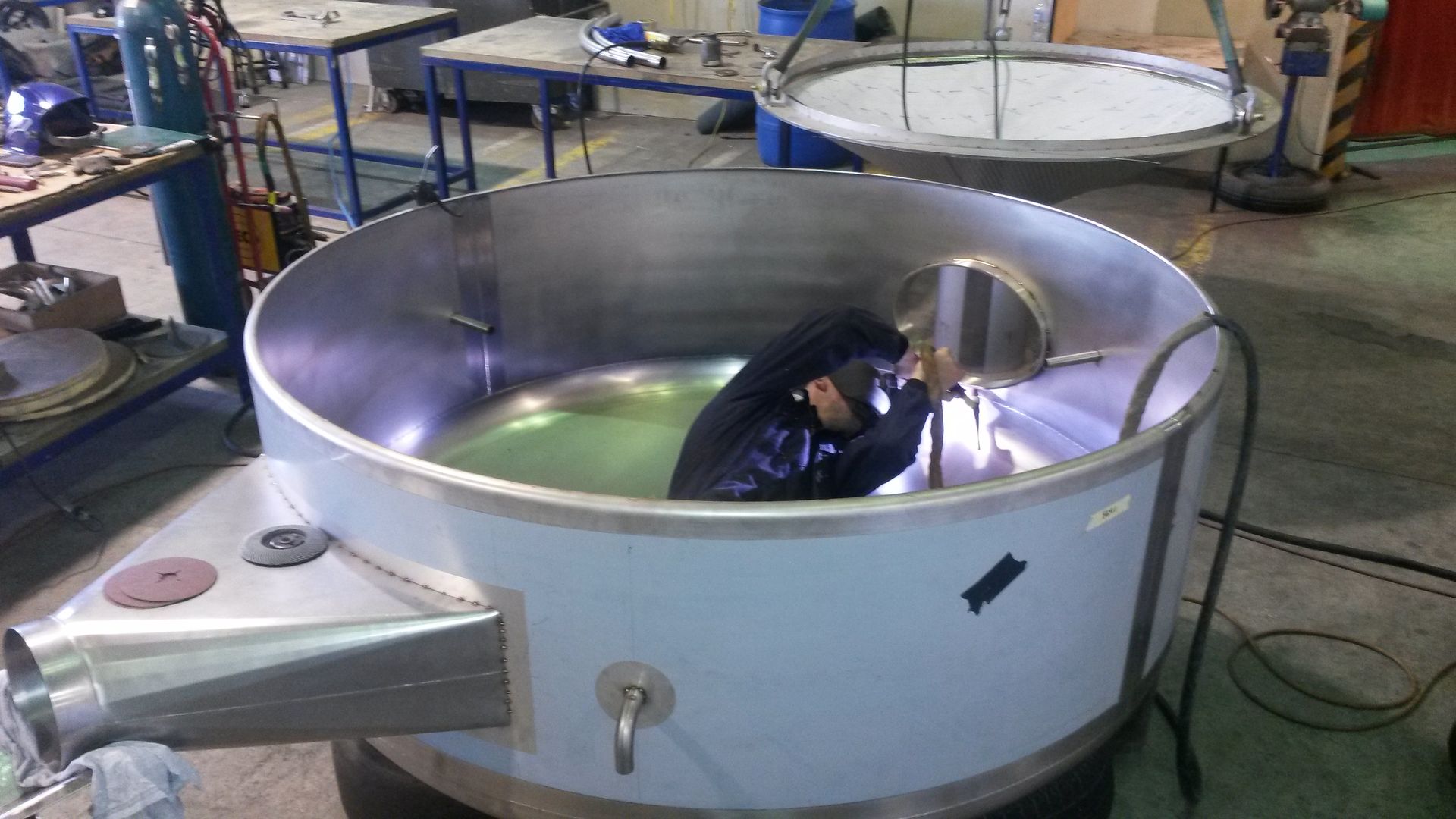 Metal pipes with a blue valve, outdoors. Green field and buildings in the background.