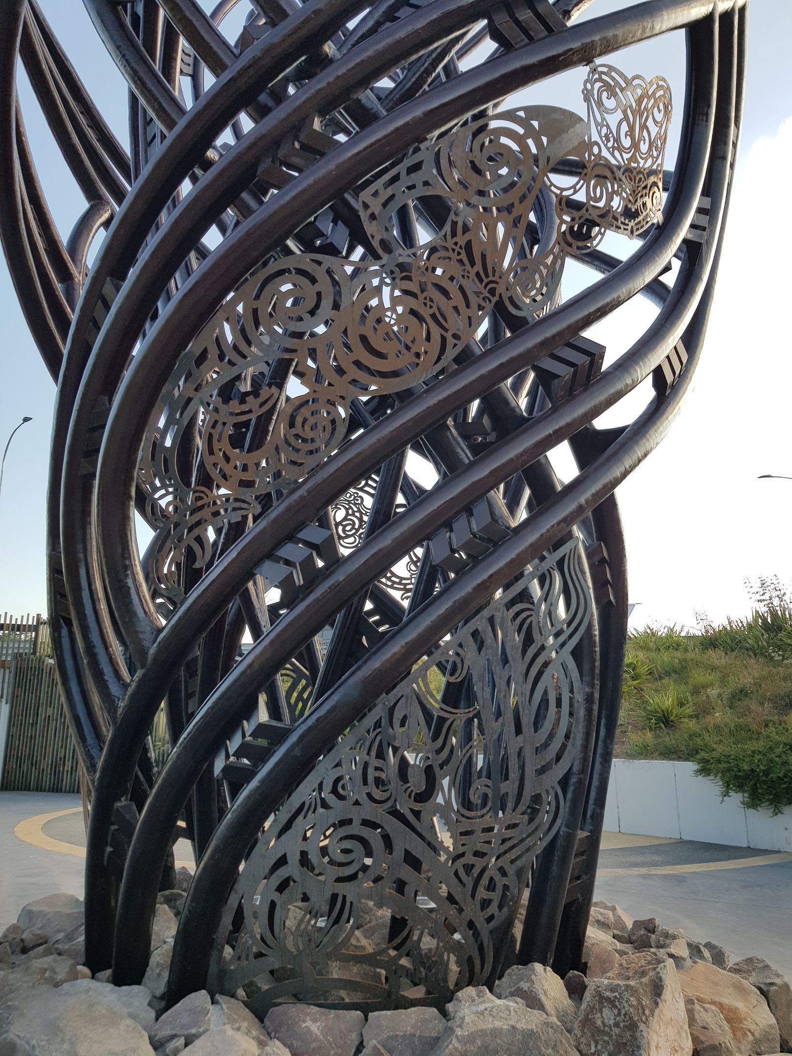 Abstract metal sculpture with swirling bars and cut-out designs, on a stone base.