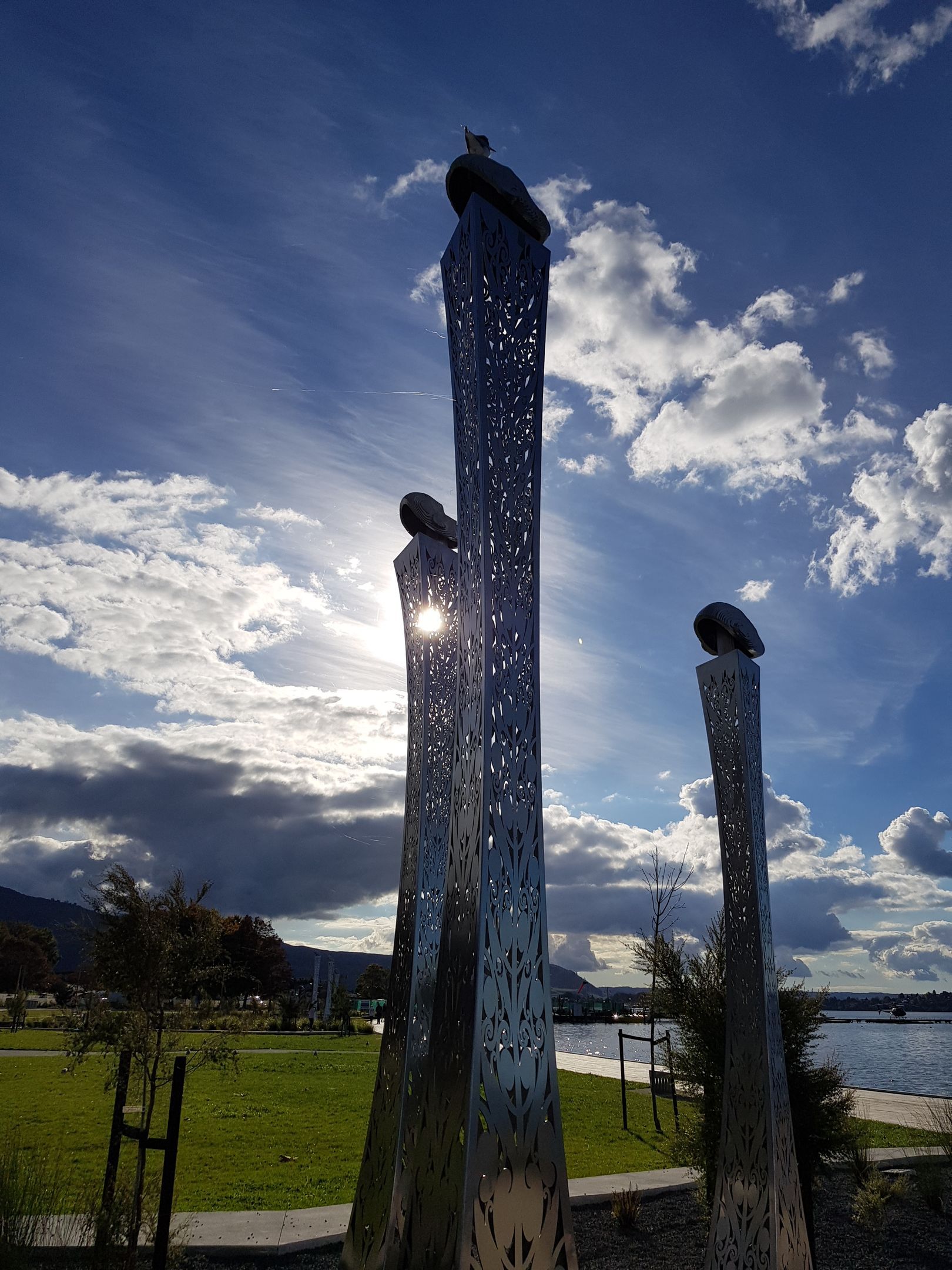 Sculptures with cutouts, topped with bird figures, silhouetted against a bright, cloudy sky.