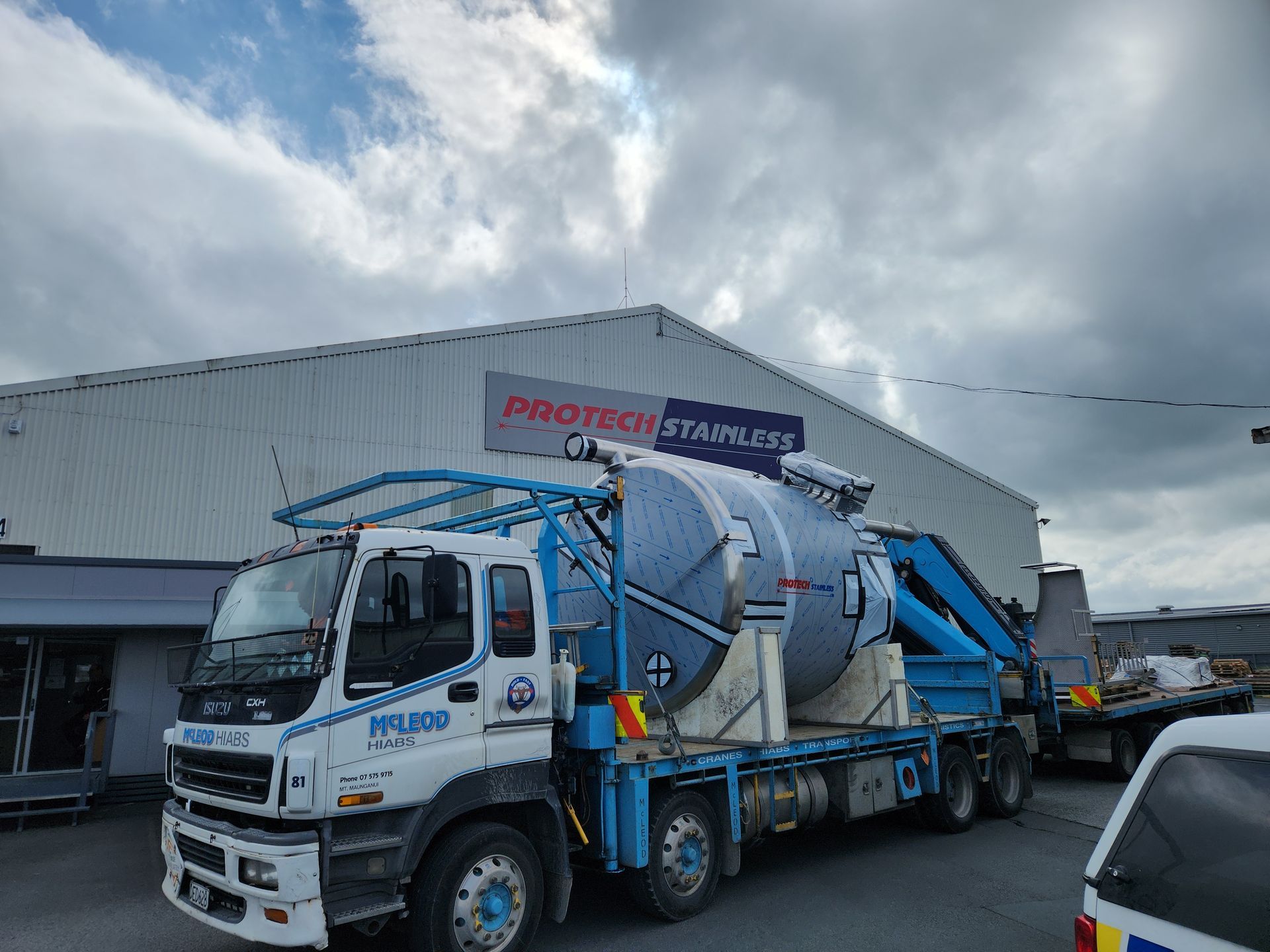 Metal pipes and valves connected to a cylindrical tank, set outdoors against a cloudy sky.