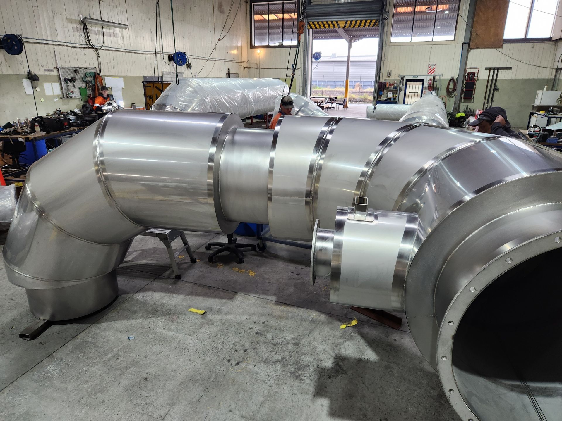 Large stainless steel industrial piping system in a workshop setting.