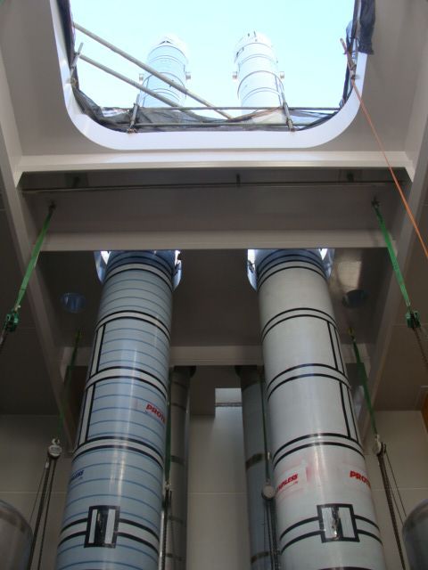 Two tall, cylindrical structures inside a white compartment, viewed from below. They have blue and white stripes and are suspended by green straps.