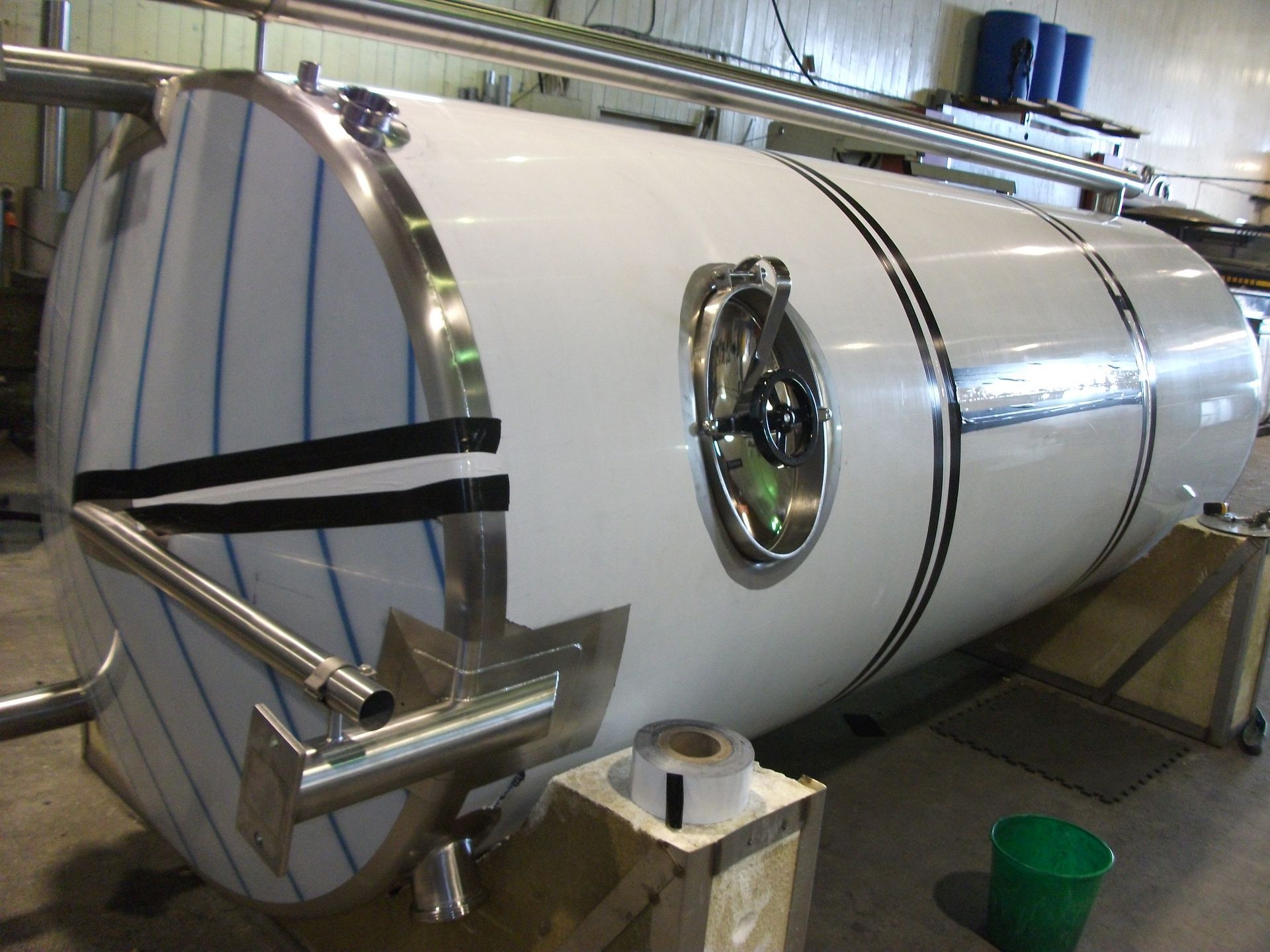 Large white industrial tank with stainless steel fittings, in a workshop.