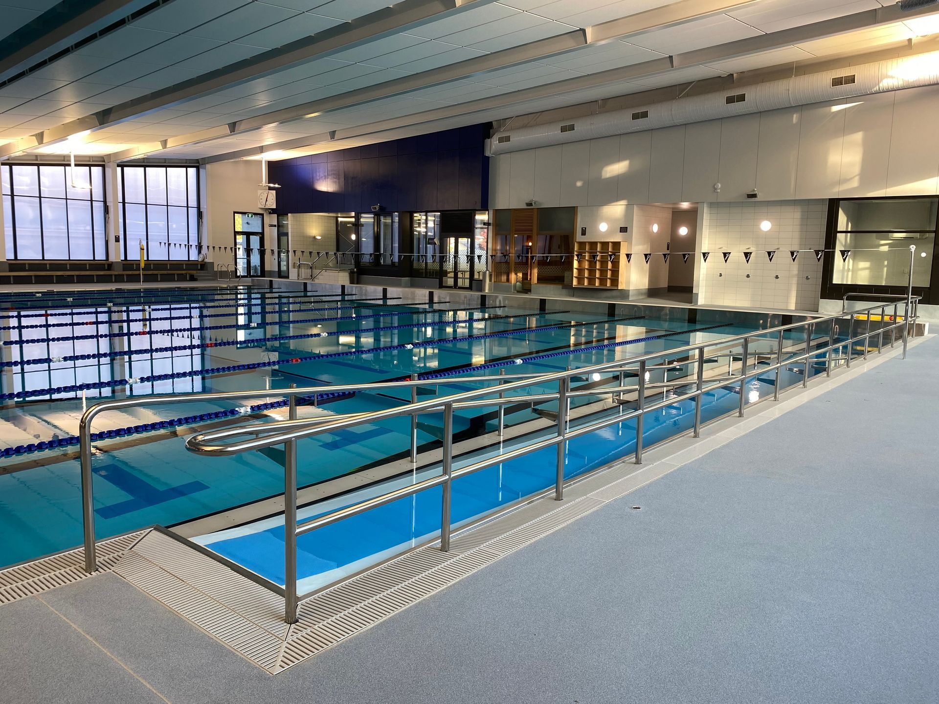Indoor swimming pool with lanes, blue water, and accessible ramp with railings.