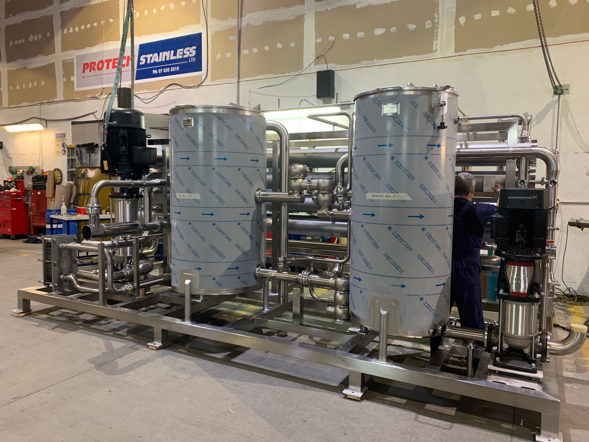 Stainless steel industrial water filtration system with piping and tanks; a person works on it.