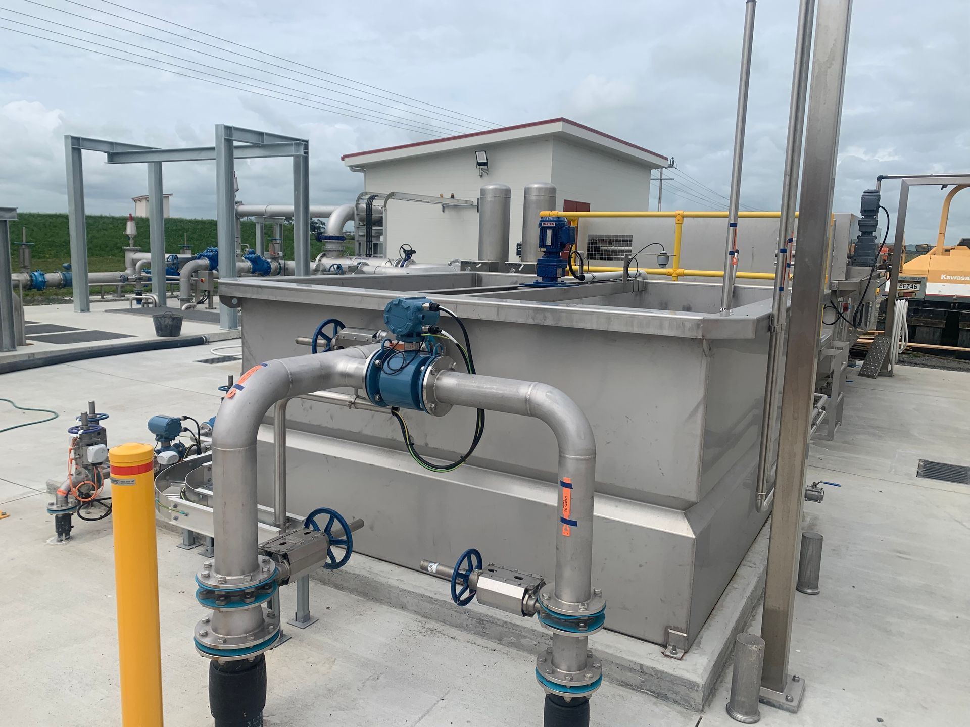 Industrial water treatment system with tanks, pipes, valves, and a small building in an outdoor setting.