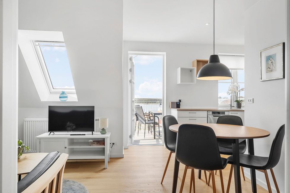 Lys og luftig spiseplads med bord, stole og udsigt over balkonen og havet.