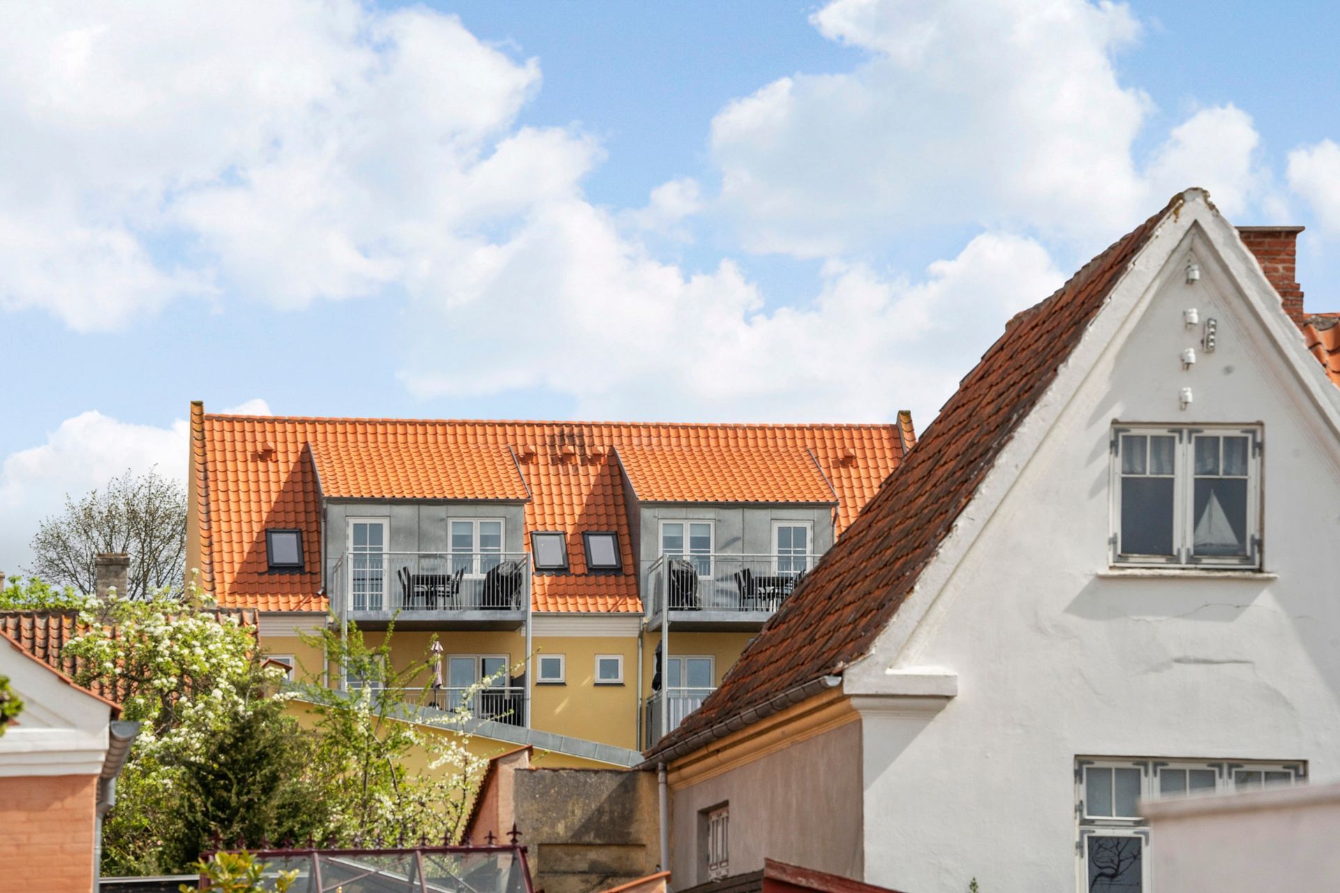 Bygninger med orange tegltage og hvide vægge under en delvist overskyet blå himmel.