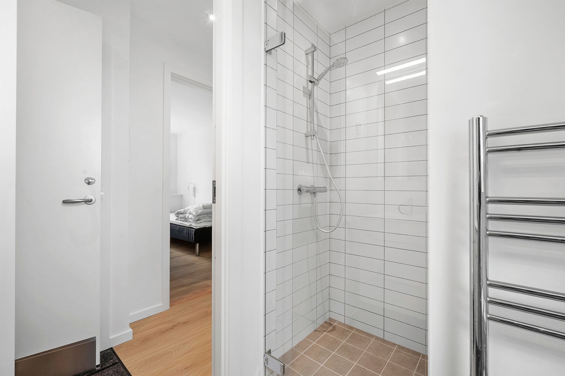 Et moderne badeværelse med glasbruser, hvide vægge og en forkromet håndklædeholder.