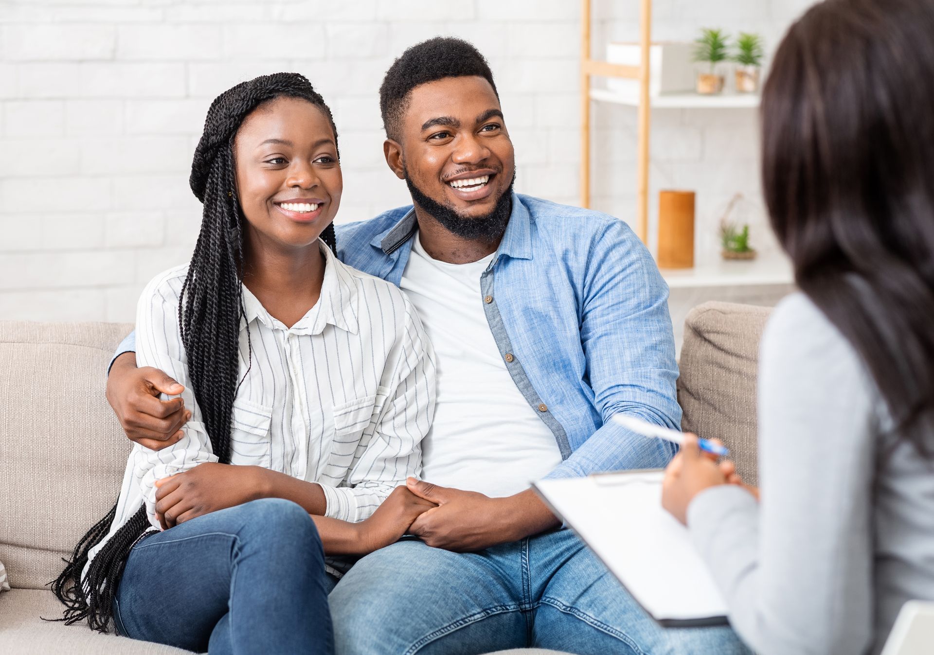 Couple on a couch smiles at a therapist who is holding a clipboard.