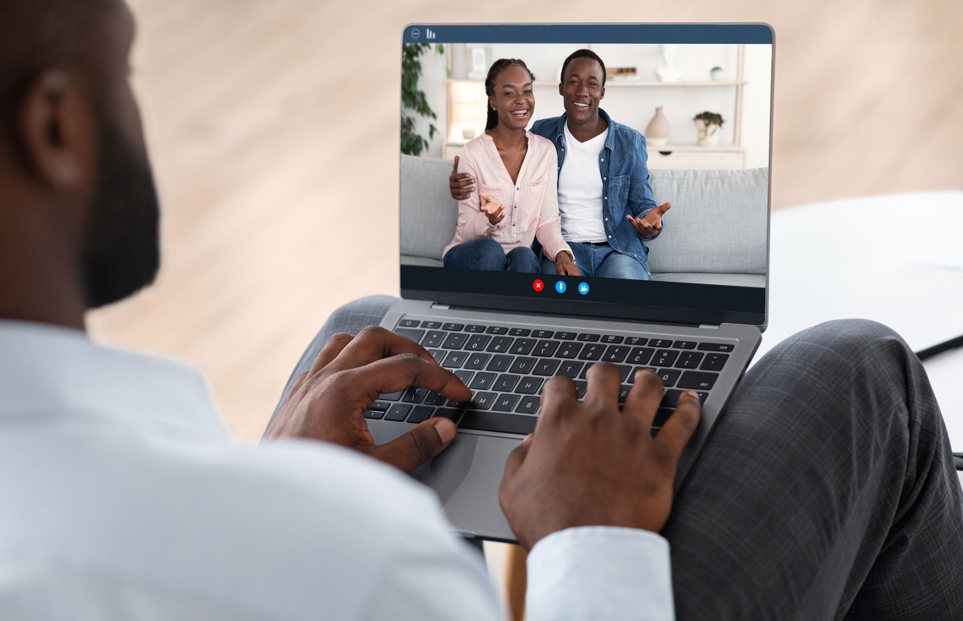 Person using laptop, video call with couple on screen, hands typing, sitting indoors.